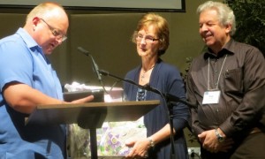 Retiring BCMB director of administration Marilyn Hiebert receives a "grandma" gift from moderator Ron van Akker as husband Rudy looks on. And, oh - something in an envelope.