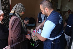 A DFATD-funded project with MCC's partner organization Middle East Council of Churches (MECC) provides non-food items for internally displaced people and vulnerable host communities in Syria's Daraa Governorate. A MECC staff person shows the contents of an aid kit to a recipient who was randomly selected to give her opinion about the items being distributed. Names are not used for security reasons. (MECC photo/Jalal Al-Eid)