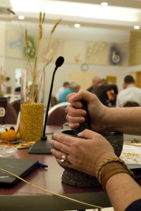 An MCC Canada 2016 annual general meeting delegate grinds wheat kernels with a mortar and pestle during a worship session. MCC photo/Rachel Bergen