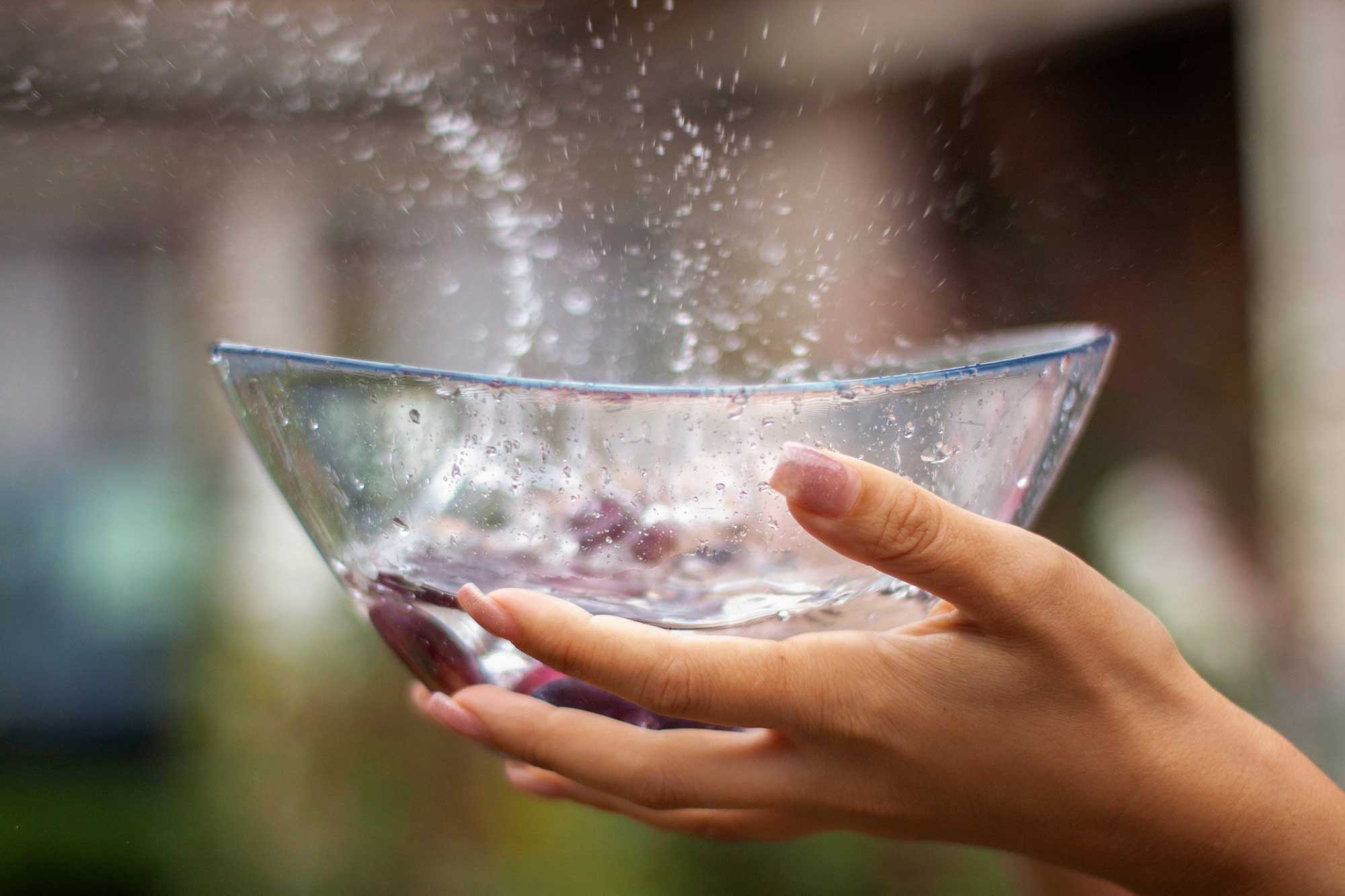 Hands holding a bowl as water splashes into it.